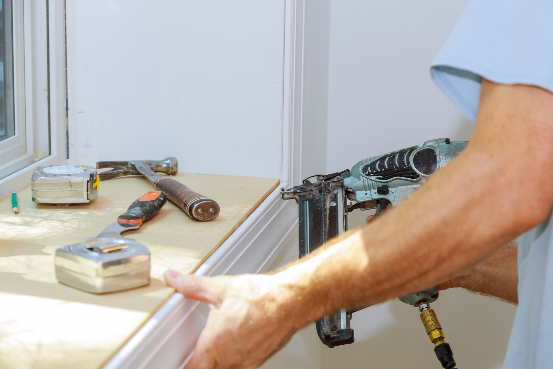 Carpenter using air nail gun to moldings for window